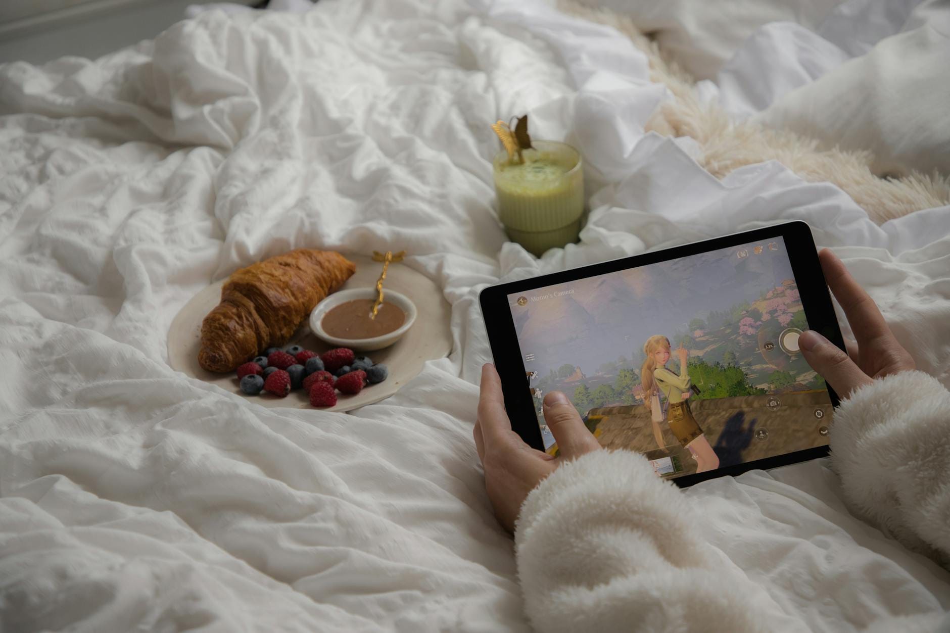 Śniadanie w łóżku z tabletem z grą MMO, rogalikiem i matcha latte
