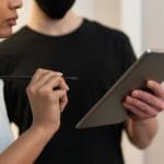Dwie osoby analizują dane na tablecie z rysikiem w biurze