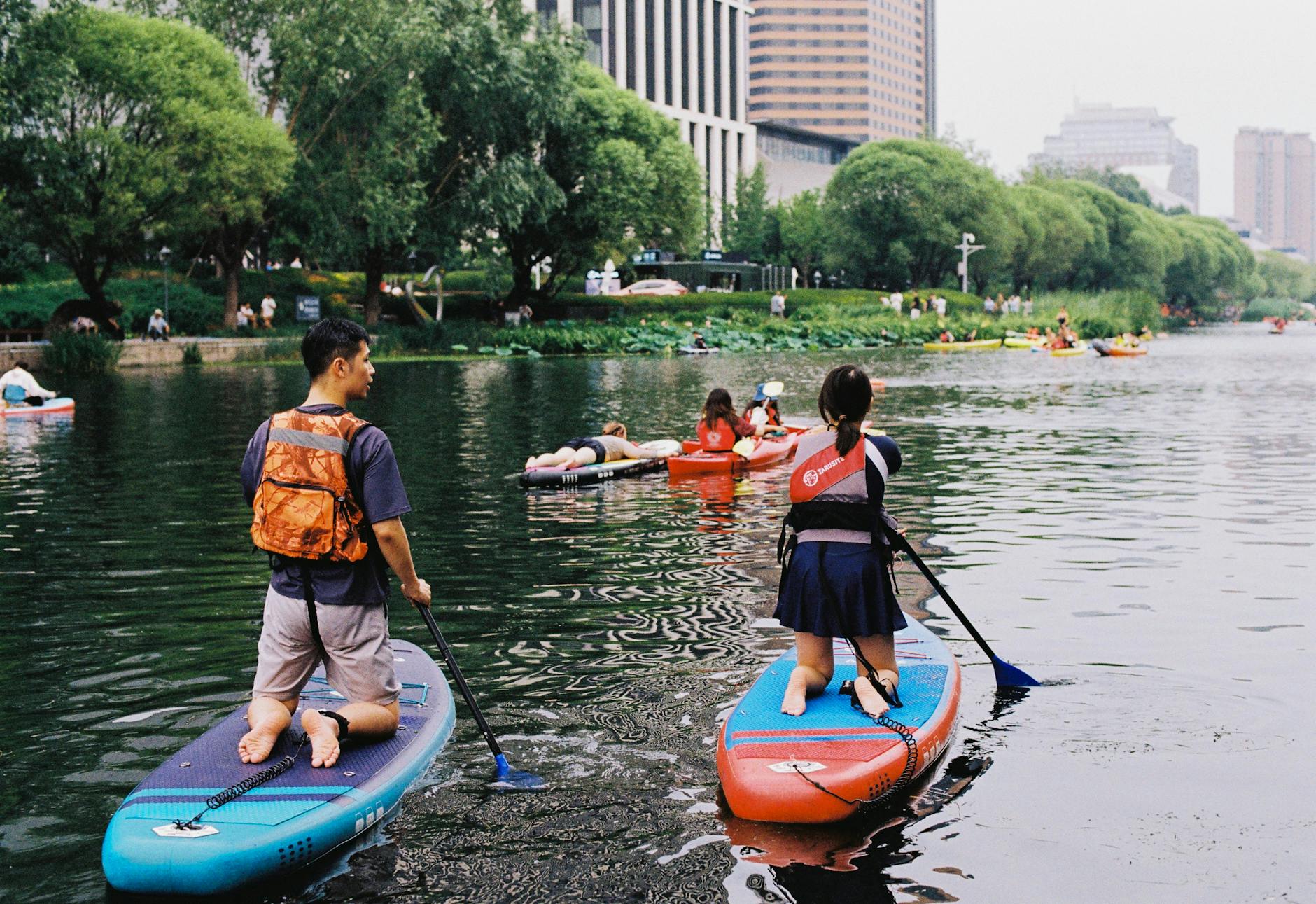 Dorośli i dzieci na deskach SUP płyną po spokojnej rzece w parku
