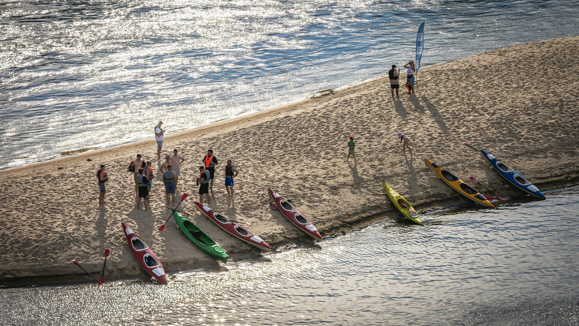 Grupa kajakarzy szykuje kajaki na piaszczystej plaży nad rzeką