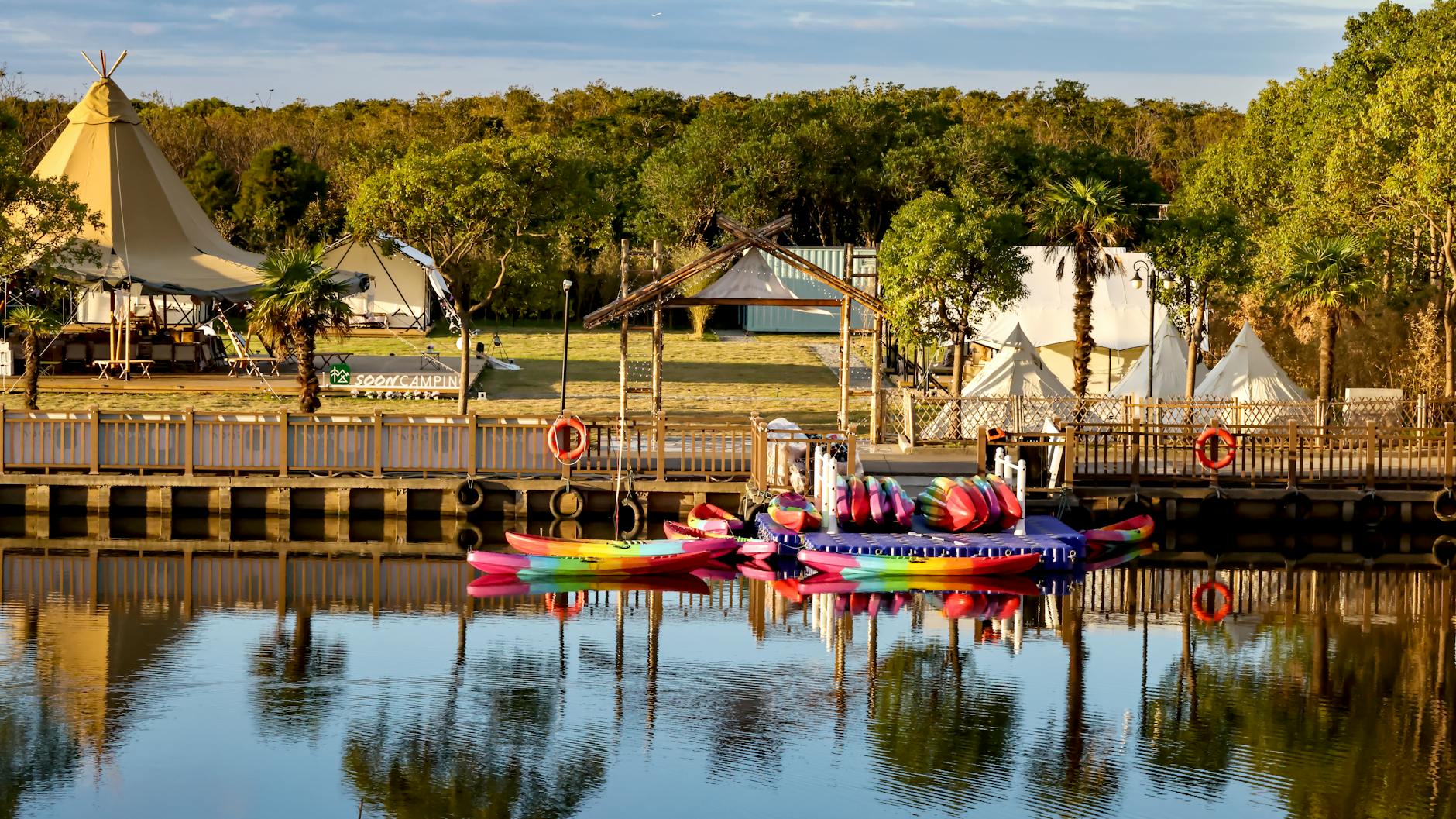 Kolorowe kajaki przy biwaku nad wodą z namiotami wśród zieleni